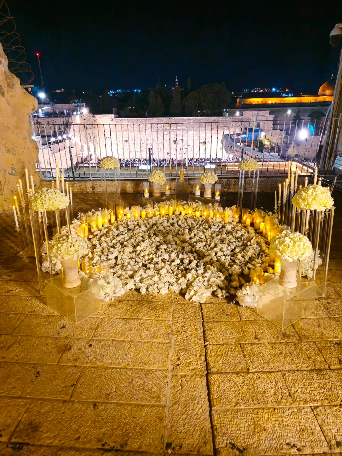 מעגל פרחים ונרות מול הכותל בלילה